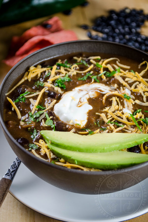 A bowl of Chili Mole with avocado, sour cream, and shredded cheese