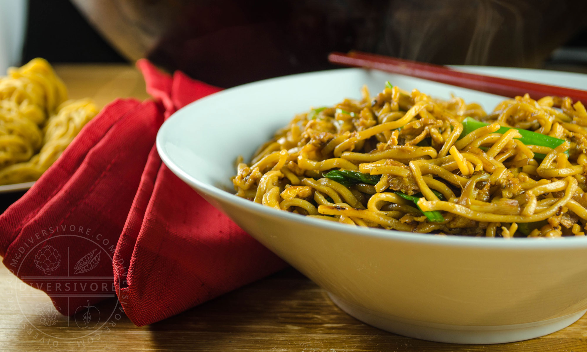Soy sauce fried noodles in a white bowl with red chopsticks and a folded red napkin