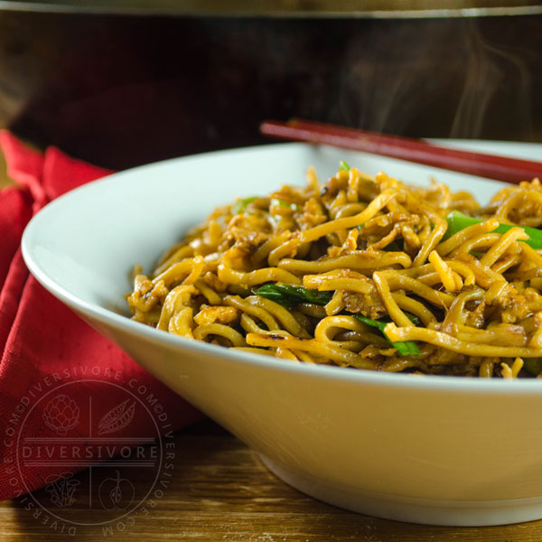 Soy sauce fried noodles in a white bowl with red chopsticks and a folded red napkin