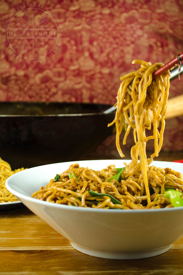 Chopsticks holding soy sauce fried noodles above a bowl