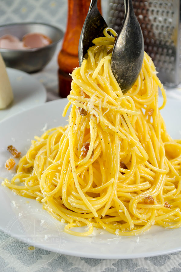 Spaghetti Carbonara with guanciale, being placed on a plate with tongs