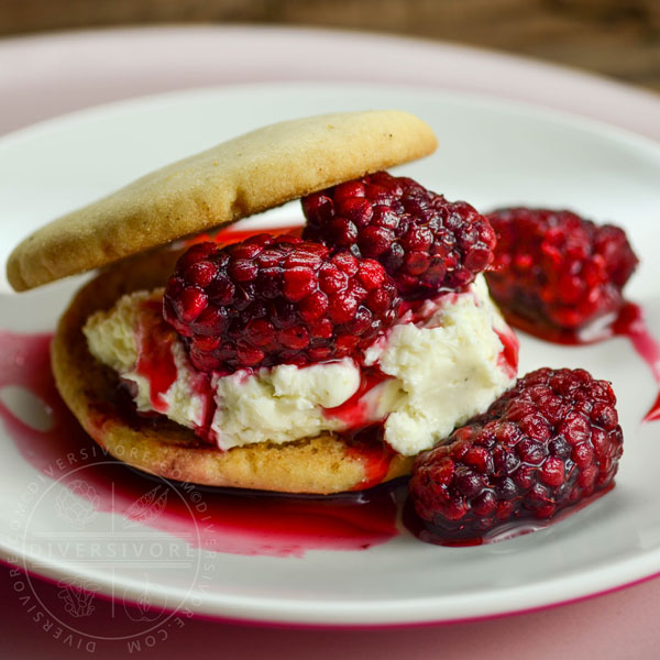 Two cookies sandwiching tayberries and sweet cream cheese on a small white plate