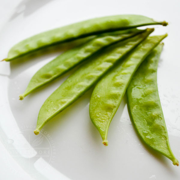 Snow pea pods spread out on a white plate