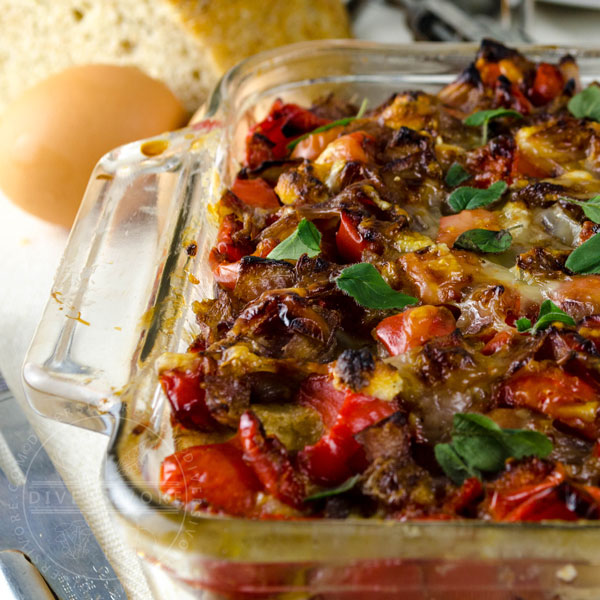 Goat cheese and emmental strata with peppers and onions sauteed in red wine in a glass casserole dish