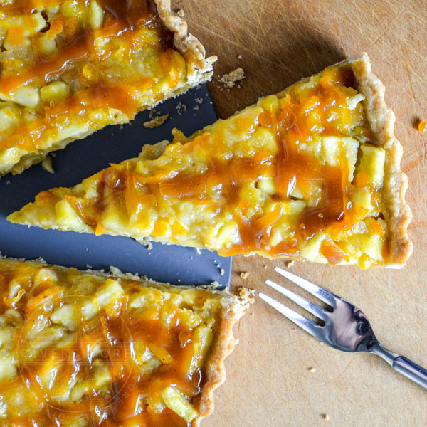 A slice of kumquat apple tart with whiskey caramel being removed from the tart pan