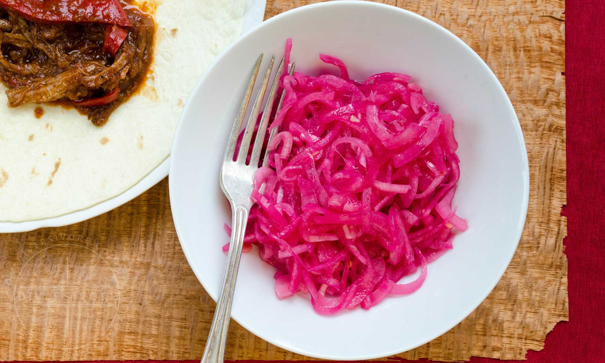 Mexican Pickled Red Onions in a white bowl, shown with a silver fork