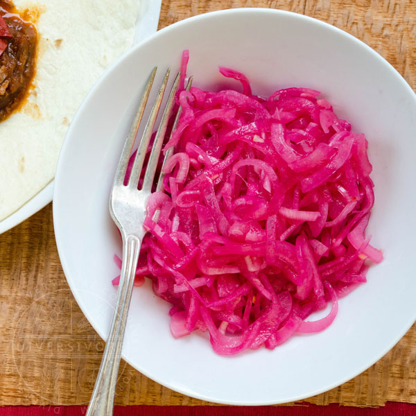 Mexican Pickled Red Onions in a white bowl, shown with a silver fork