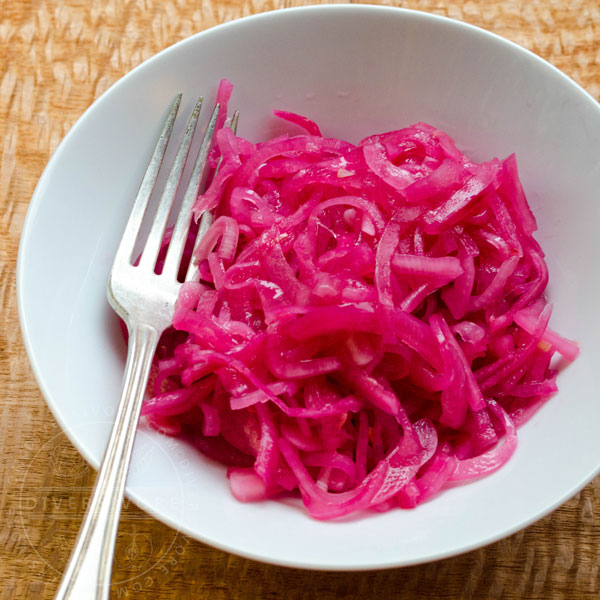 Mexican Pickled Red Onions in a white bowl, shown with a silver fork