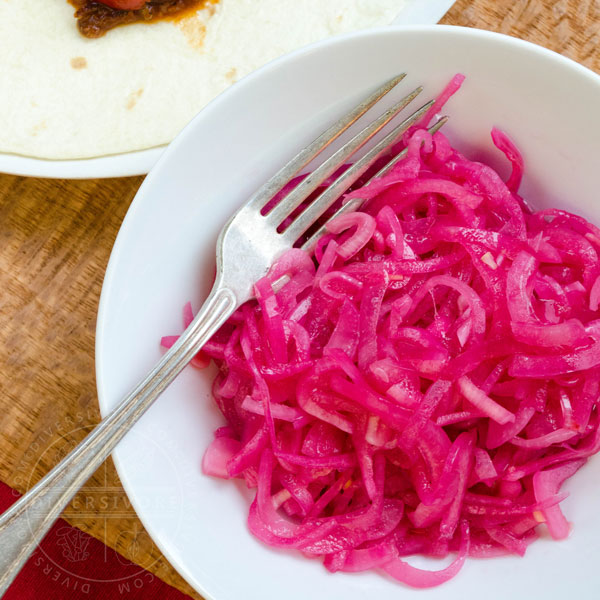 Mexican Pickled Red Onions in a white bowl, shown with a silver fork