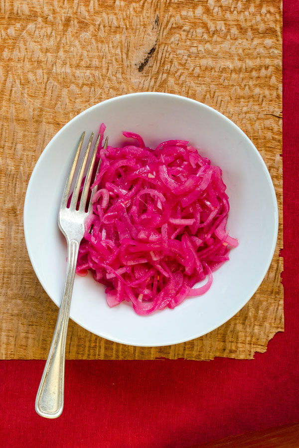 Mexican Pickled Red Onions in a white bowl, shown with a silver fork