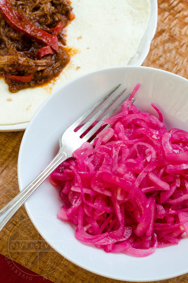 Mexican Pickled Red Onions in a white bowl, shown with a silver fork, served with Mexican shredded beef