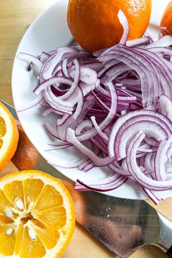 Sliced red onions on a plate with whole and halved bitter (Seville) oranges