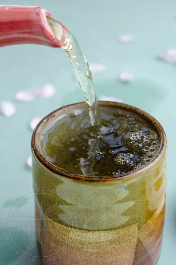 A tea pot pouring green tea into an ornate Japanese tea cup