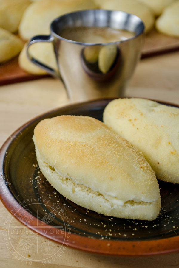 Pandesal with butter on a plate in front of a coffee cup