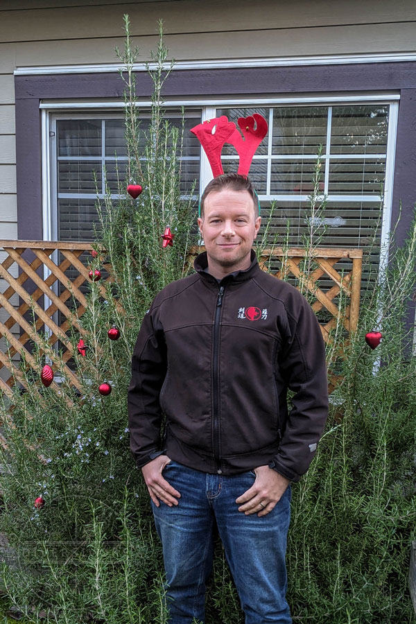 Sean standing in front of his gigantic rosemary plant with Christmas decorations