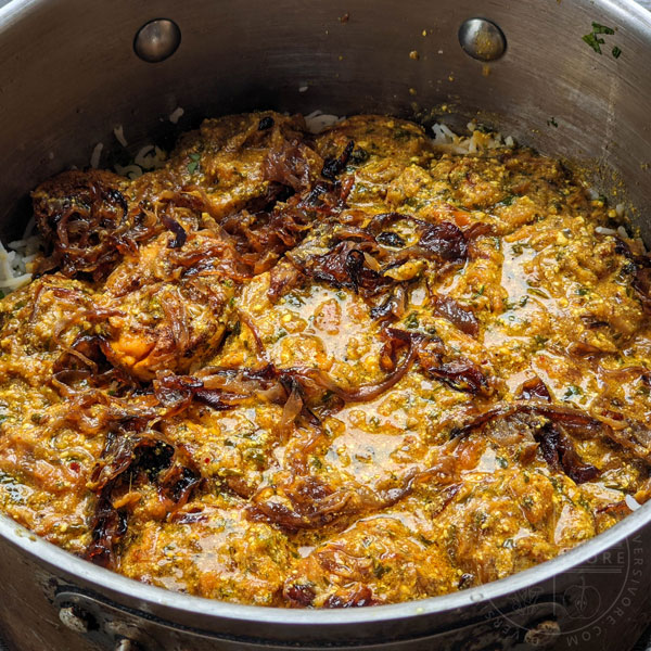 Hyderabadi egg biryani layered with gravy and fried onions, ready for another layer of rice