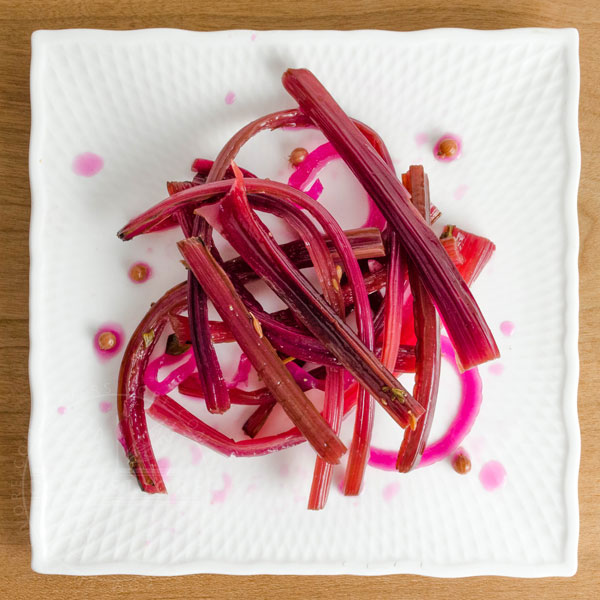 Spicy beet stem pickles on a white square plate