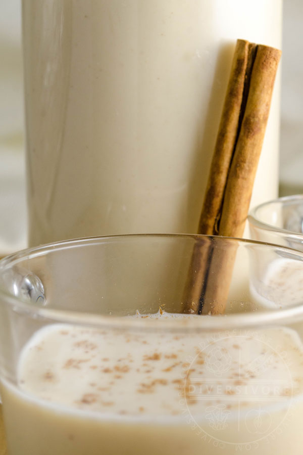 Coquito in a glass and bottle with a cinnamon stick