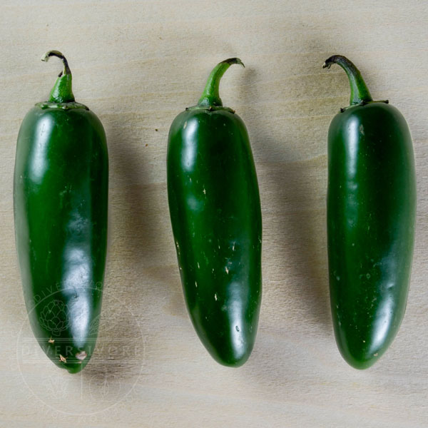 Trio of green jalapeño peppers on a wood background